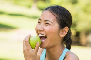 Happy woman eating an apple outside Dr. Joe Thomas Dentistry